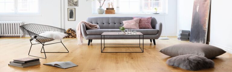 Ein Wohnzimmer mit einer grauen Couch, Kissen und einer kunstvoll bemalten Fassadengestaltung. Thomas Jung Maler- & Stukkateurbetrieb aus Spiesen